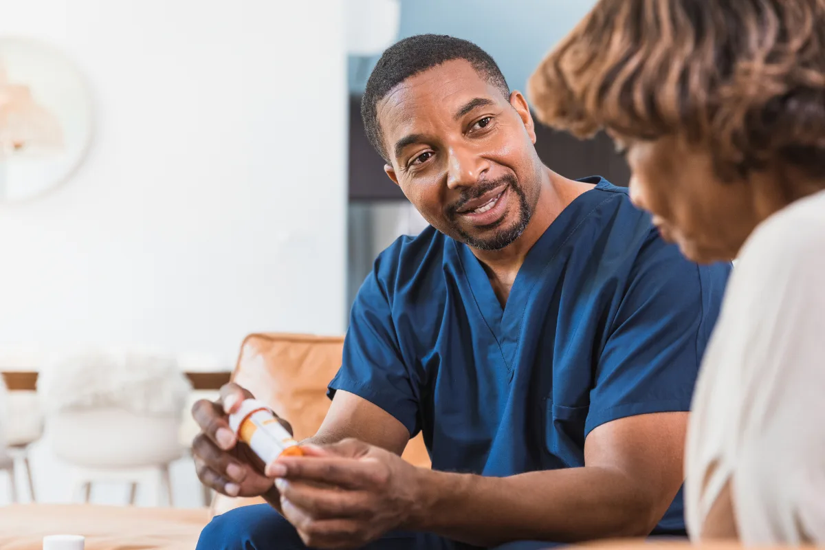 A medical professional in blue scrubs discusses a prescription with a patient, conveying a sense of care and attention in a cozy setting.